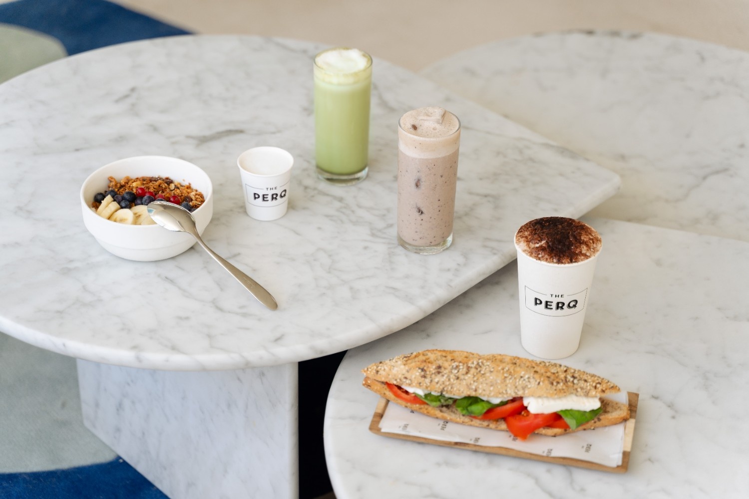 a sandwich, drinks, coffees and a bowl with breakfast food on a table