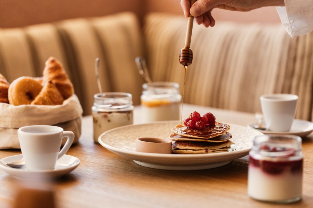 table with multiple breakfast options including pancakes with honey and croissants
