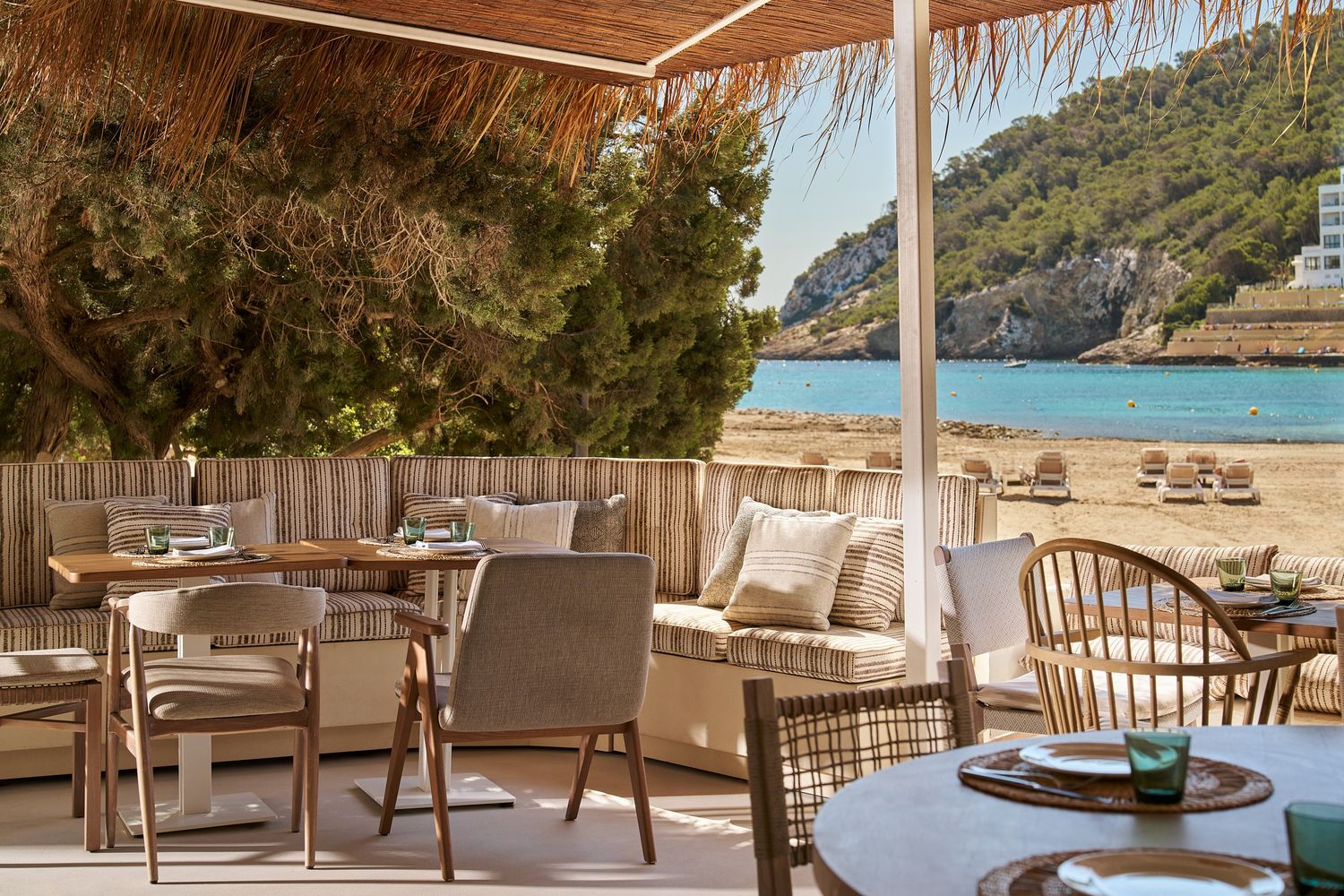 image of outside terrace of a restaurants with multiple tables and chairs and the sea in the background